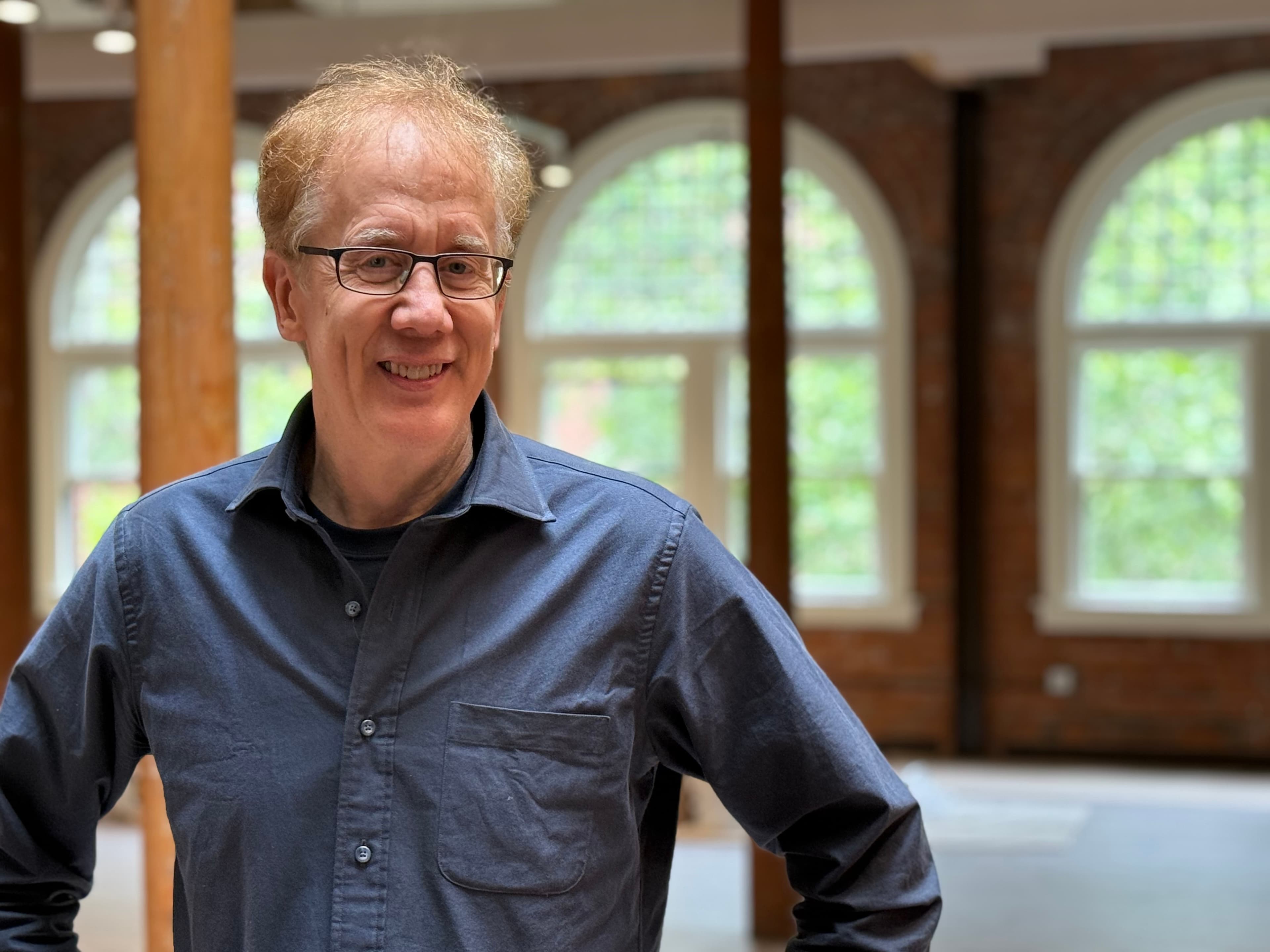 Andrew Conru standing in the Occidental Fine Arts Center gallery in front of arched windows, summer 2025
