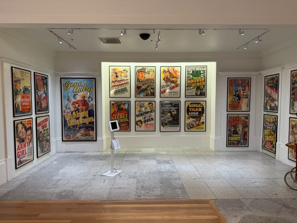 A Coliseum gallery room lined with colorful framed vintage movie posters under gallery lights.