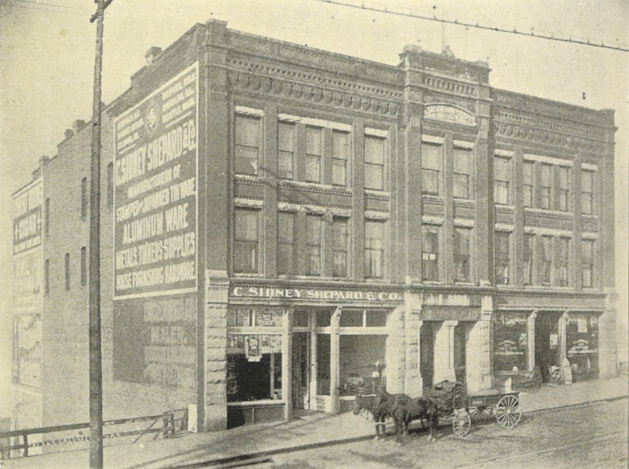The building in 1900 as the C. Sidney Shepard and Co. metalware house, horse and wagon at the curb, painted advertising on the south wall